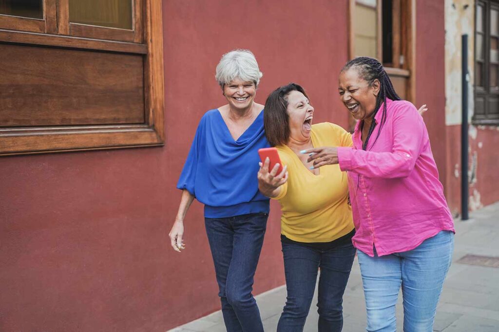 3 mature women walking in street laughing together - sense of fun Kathy Roots