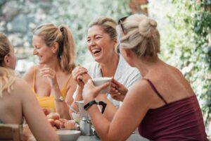 Mature women round a table eating and laughing